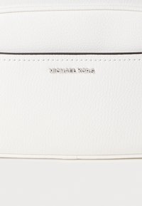 Λευκή τσάντα ώμου από υφή δέρματος με ανάγλυφο λογότυπο "MICHAEL KORS" σε ασημένιο χρώμα. Διαθέτει μινιμαλιστικό σχεδιασμό και διακριτική ραφή κατά μήκος των άκρων.