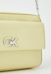 Yellow faux leather handbag with a smooth texture, featuring a silver logo clasp and a rectangular shape with a chain strap.