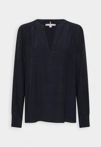Blouse noire à manches longues, encolure en V, tissu lisse, détails froncés aux épaules, coupe droite, poignets à boutons.