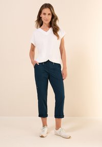 Vit kortärmad t-shirt med v-ringning, marinblå cropped byxor med fickor och uppvikta fållar, i kombination med vita skor med gröna detaljer.
