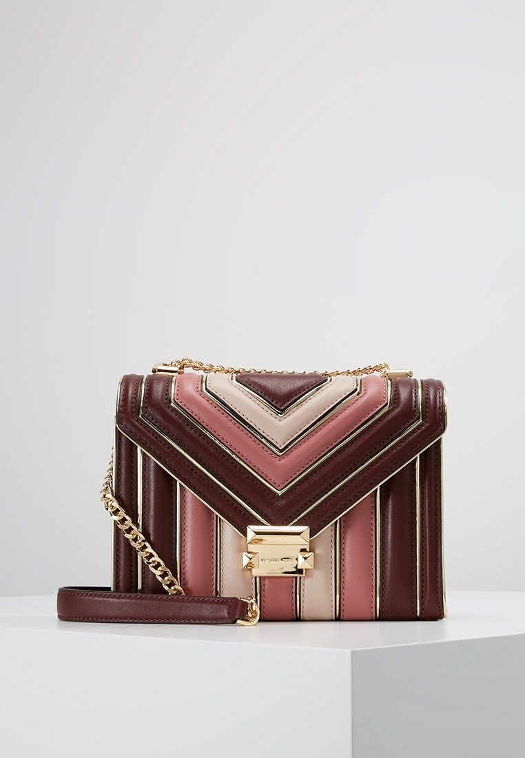 Sac à bandoulière en cuir avec motif chevron dans les tons bordeaux, rose et beige, bandoulière chaîne dorée et fermoir rectangulaire doré sur fond blanc.