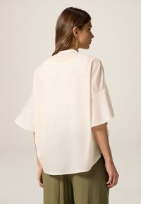 Maglietta di colore crema, dalla vestibilità ampia, con maniche corte e scollatura rotonda; presenta un tessuto texture e un design a orlo alto-basso.
