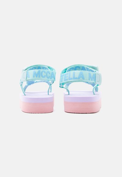 Ανοιχτό μπλε σανδάλια με φαρδιές λουρίδες που εμφανίζουν τη λέξη "MCCARTNEY." Η ανυψωμένη σόλα διαθέτει πολύχρωμη στρώση σε αποχρώσεις λεβάντας και ροζ. Ομαλή υφή.