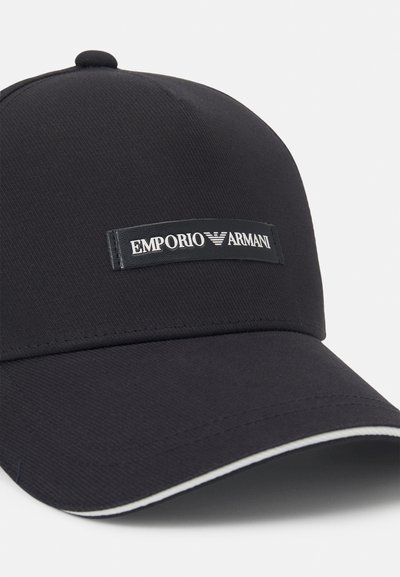 Casquette de baseball noire en tissu texturé, avec un patch logo sur le devant et un accent blanc sur la visière. Design simple et minimaliste.