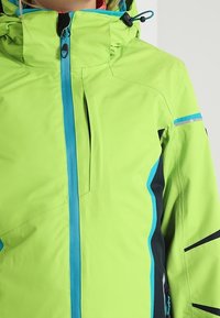Zelená nepromokavá bunda s modrými akcenty, vysokým límcem a zapínáním na zip. Texturovaná látka s černými detaily a kapsami.