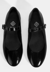Schwarze Lackleder-Mary Jane-Schuhe mit einer abgerundeten Spitze, glänzender Oberfläche und einem verstellbaren Riemen über dem Spann. Logo im Inneren sichtbar.