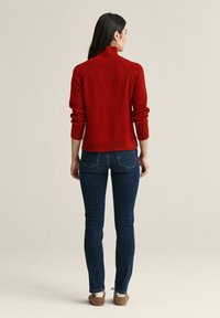 Röd, figurnära polotröja i mjukt material, med ribbade ärmslut och nederkant, kombinerad med mörka jeans och avslappnat fotfodral.