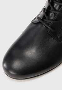 Black leather shoe with a smooth texture, rounded toe, and thin laces. The design includes a subtle sheen and streamlined silhouette.