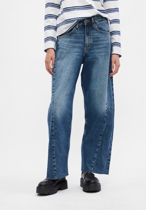 Lösa blå jeans i denim med hög midja, rå nederkant och kontrasterande sömmar. Tillsammans med en randig långärmad topp och svarta stövlar.