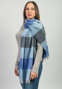 Modrý a šedý kostkovaný šátek vyrobený z jemné tkaniny, s třásněmi. Elegantly zavěšený přes rameno, ukazuje směs světlých a tmavých tónů.