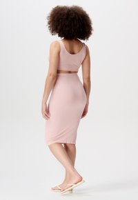 Rosa ribbad crop top och tight midi kjol set, med en slät textur, breda remmar och en midjelång skärning, i kombination med minimalistiska flip-flop-sandaler.