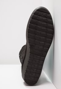 Svart sneaker med en strukturerad gummisula och en framträdande mönstring. Har en lätt klack och stickade detaljer.