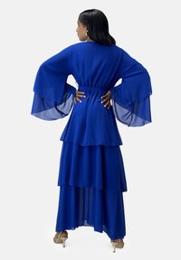 Lang blå kjole lavet af letvævet stof med lagdelte lag. Den har brede klokkeærmer og et bælte i taljen, der tilføjer struktur og bevægelse.