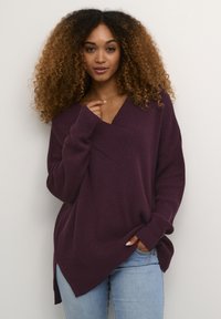 Tekstureret, dyb lilla oversized sweater med V-halsudskæring, ribbet stof og slids i siden. Sammen med lys blå jeans.