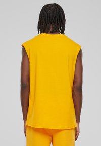 Ärmløs gul bomulds T-shirt med rund halsudskæring, afslappet pasform og let buet kant. Ingen synlige mønstre eller hardware.