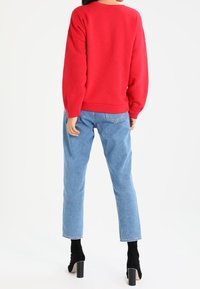 Rode sweatshirt met een relaxed fit, verlaagde schouders en geribbelde manchetten, gecombineerd met lichtblauwe rechte jeans en zwarte blokhakken.