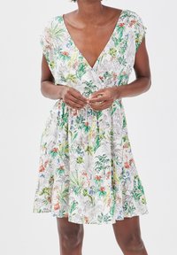 Sukienka w kwiatowy wzór z lekkiej tkaniny, z głębokim dekoltem w serek, krótkimi rękawkami typu "cap sleeves" oraz elastyczną talią. Kolory obejmują biały, zielony i pomarańczowy.