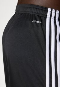 Shorts de sport noirs avec un design à trois bandes blanches, dotés d'une taille élastique et du logo AEROREADY. Tissu lisse et léger.