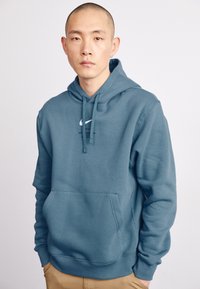 Sweatshirt com capuz em azul, feito de tecido suave. Apresenta um bolso frontal, punhos canelados e um logótipo branco no peito. Design simples e casual.