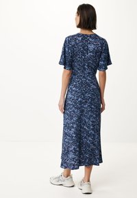 Modré květinové midi šaty s krátkými zvonovými rukávy, vyrobené z měkké látky, s rozšířeným lemem. Nosené s bílými sportovními teniskami.
