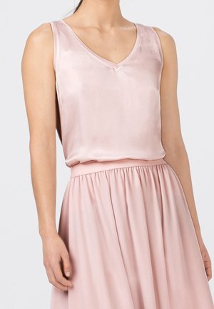 Femme portant un haut sans manches en satin rose clair à col en V, rentré dans une jupe froncée taille haute en tissu assorti.