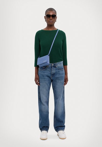 Green knit sweater, loose light blue jeans, white sneakers, and a small blue crossbody bag. Black sunglasses and hoop earrings complete the look.