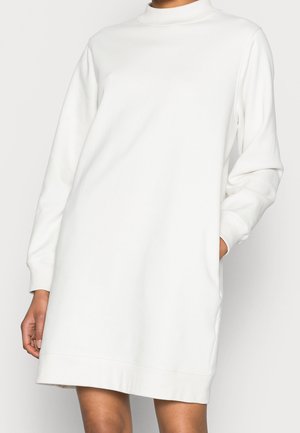Robe blanche à manches longues en tissu doux, avec un col haut, une coupe décontractée et des poches latérales, dont l'ourlet arrive au milieu de la cuisse.