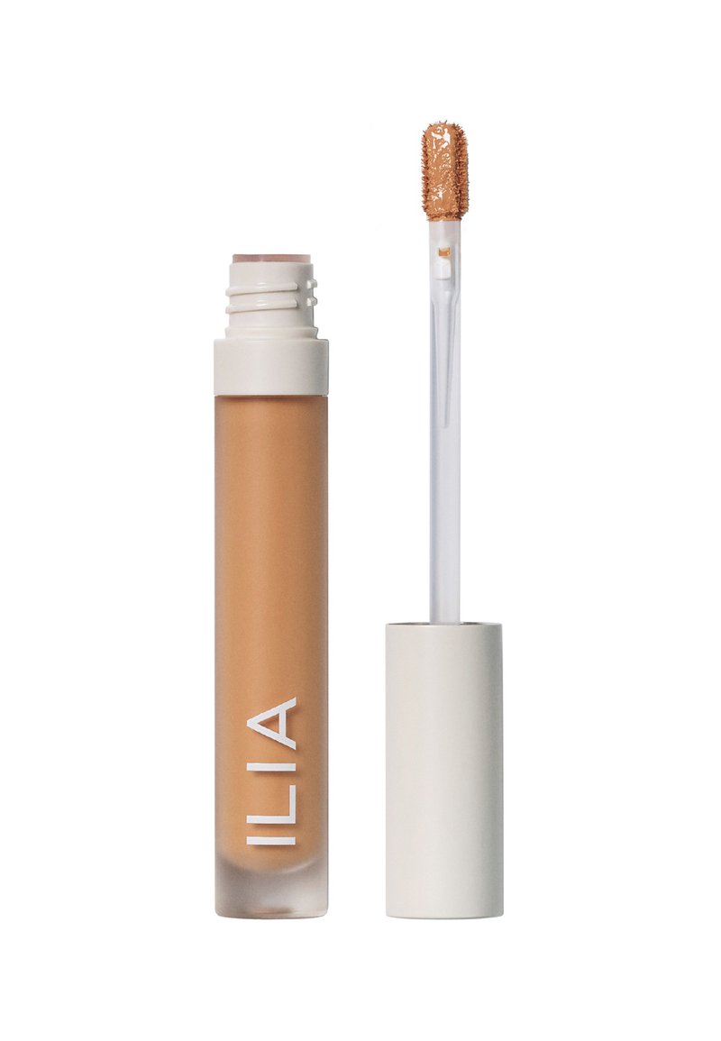 ILIA concealer i en klar, frosted tube med en beige formel, som har en teksturert applikatorpinne og et hvitt lokk.