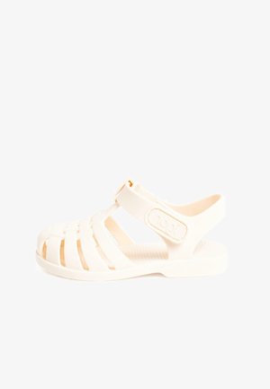 Valge plastist sandaal, millel on rihmadega disain, reguleeritav pahkluu rihm, tekstureeritud tallal ja kerge, avatud toe konstruktsioon.