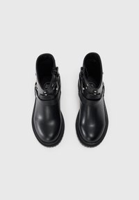 Botines negros con un acabado de cuero liso, que cuentan con un cierre lateral, una correa decorativa con tachuelas de metal y una puntera redonda.