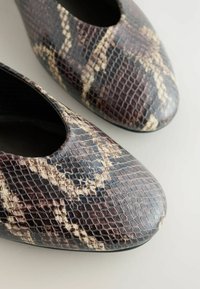 Ballerines imprimées serpent marron et noir avec un bout rond, mettant en valeur des détails de surface texturée sur un fond clair.