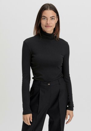 Maglione a collo alto nero con maniche lunghe, realizzato in materiale morbido, abbinato a pantaloni neri a vita alta con chiusura a un solo bottone.