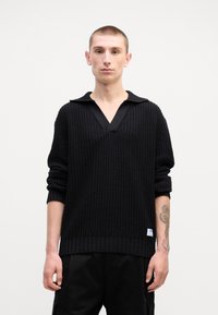 Schwarzer Strickpullover mit strukturiertem Muster, tiefem V-Ausschnitt und kontrastierendem Kragen. Verfügt über gerippte Bündchen und ein kleines Etikett am Saum.