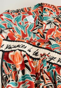 Farebná pyžamová súprava s tropickým potlačou siahajúcou po zelené, oranžové a čierne listy a kvety, s preloženým golierom a elastickým pásom s textom v písme.