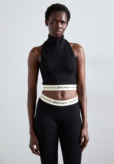 Crop top tricot noir avec col haut et leggings taille haute assortis, présentant des bandes blanches avec le logo "Palm Angels" à la taille.