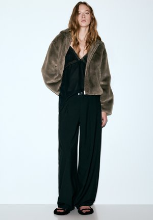 Hnedá bunda z umelej kožušiny so zipsovým zapínaním, na čiernom saténovom topu, doplnená o široké čierne nohavice a chlpaté čierne papuče.