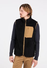 Juodas fliso liemenė su šviesiai rudos spalvos izoliacijos intarpu, užtrauktuko uždarymu ir krūtine kišene. Audinys turi tekstūrišką, jaukią išvaizdą.