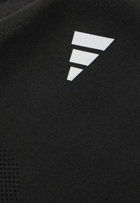 Tissu noir avec un motif texturé. Présente un logo blanc composé de trois triangles ascendants, positionné dans le coin inférieur droit.