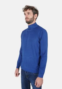Maglione a collo alto blu realizzato in tessuto morbido con un design aderente. Presenta maniche lunghe e collo e polsini a costine. Abbinato a jeans scuri.