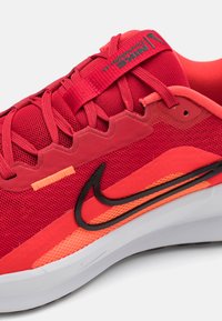 Baskets de sport rouges avec une tige en mesh, des accents noirs et oranges contrastants, une semelle texturée et un logo swoosh distinctif.