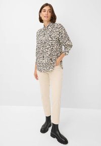 Zwarte en beige luipaardprint overhemd, met knopen en een kraag, gecombineerd met crèmekleurige broeken en zwarte enkellaarzen. Soepele stof, slim fit.