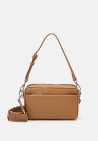Sac bandoulière beige fabriqué en matériau lisse, avec un compartiment zippé, une sangle réglable et le logo Calvin Klein à l'avant.