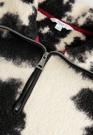 Fleece-Pullover mit schwarz-weißem Kuhmuster, Reißverschluss und kontrastierendem roten Innenkragen. Weicher, strukturierter Stoff mit einem glatten Reißverschluss.