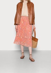 Brun læder skjortejakke, beige bluse, lyserød blomsteret flerlagsskort, brune sandaler, flettet taske. Har en glat tekstur og lagdelt design.