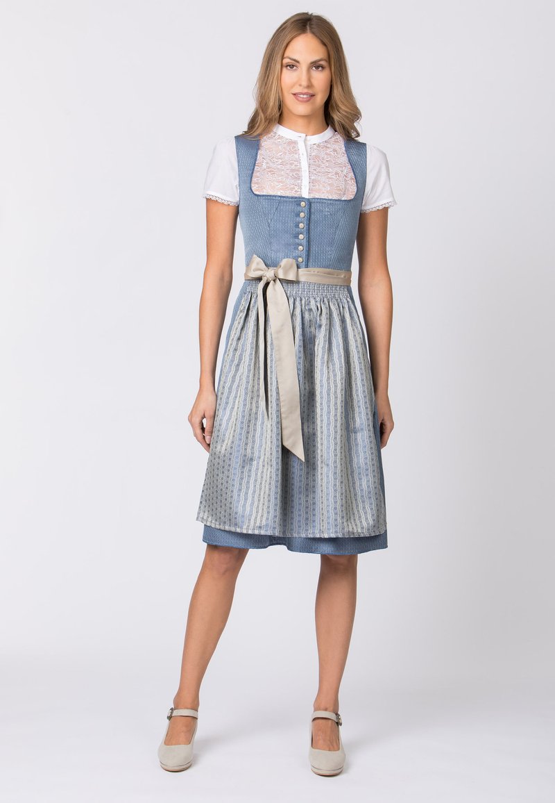 Traditionelles Kleid mit einem blauen karierten Oberteil, einer weißen Spitzenbluse darunter und einem gemusterten blau-silbernen Rock mit einer beigen Ripsbandbindung.