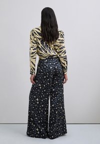 Camiseta de manga larga con un patrón de rayas de tigre en amarillo y negro, combinada con pantalones de pierna ancha con un estampado de leopardo en negro y dorado. Textura de tela suave.