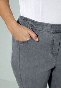 Szare spodnie z elastycznym pasem, z bocznymi kieszeniami, wykonane z miękkiego materiału przypominającego dżins. Gładka tekstura z widocznymi detalami szwów.