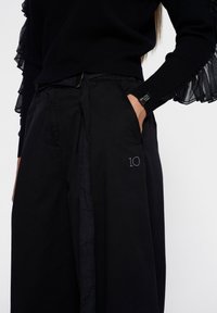 Zwarte wijde broek met een gladde textuur, voorzien van een geborduurd '10' op de zak en vergezeld van een zwart top met ruches.