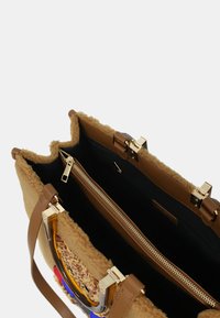 Borsa a mano marrone con un esterno in morbido tessuto testurizzato, hardware dorato e un interno nero a contrasto dotato di una tasca con zip. Manici trasparenti.