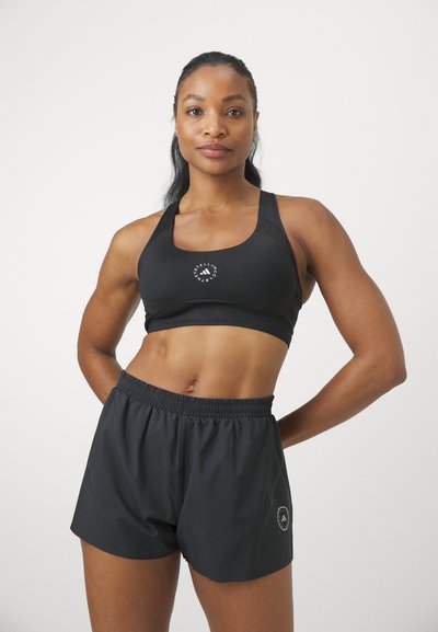 Sostén deportivo negro con un logo redondo en el centro y detalles de malla, combinado con pantalones cortos negros de corte suelto que tienen una cintura elástica y un acento de logo.
